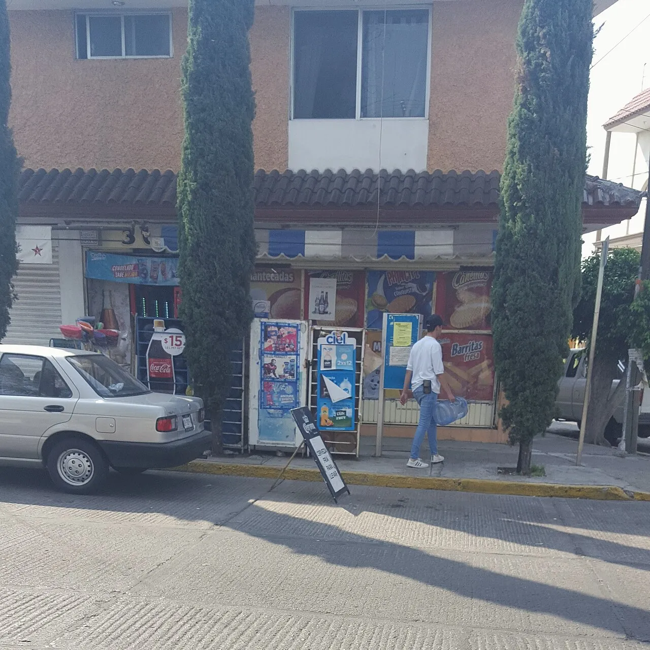 Fachada de una tienda de abarrotes en una esquina, con un auto blanco estacionado enfrente