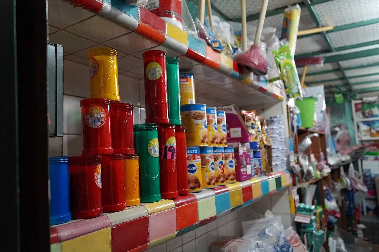 Estantes de una tienda de abarrotes con latas, botes y veladoras de colores sobre azulejo