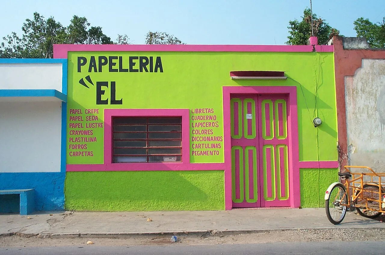 Fachada verde y rosa de una papelería con la lista de productos pintada en la pared